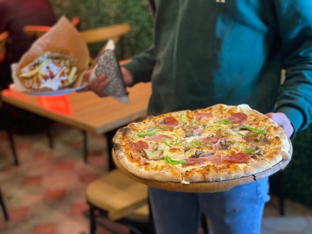 A waiter holding a pizza and a gyro pita at 3 Fiori Fast Food Vlore