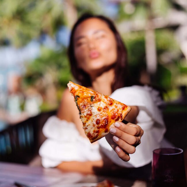A woman showing a slice of pizza with a blured background