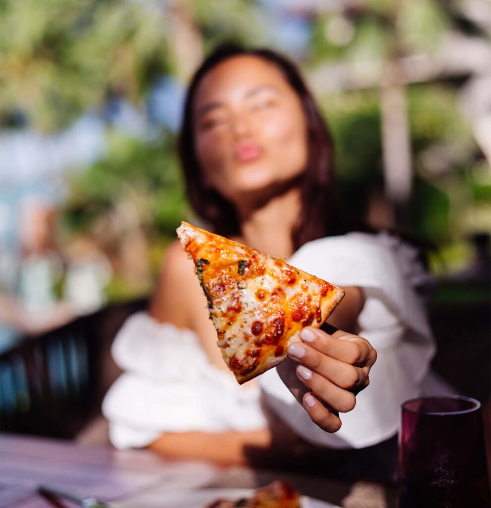 A woman showing a slice of pizza with a blured background