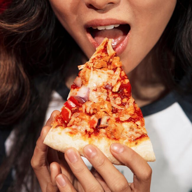 a woman opening her mouth and eating a slice of pizza