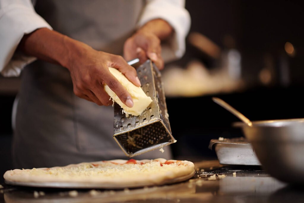 A man shredding mozarella and putting on a pizza